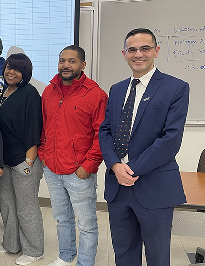 Group of people standing in a classroom, one in a suit, others in casual attire.