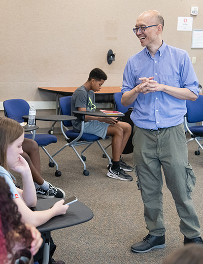 Man in blue shirt speaking to students in a classroom setting.