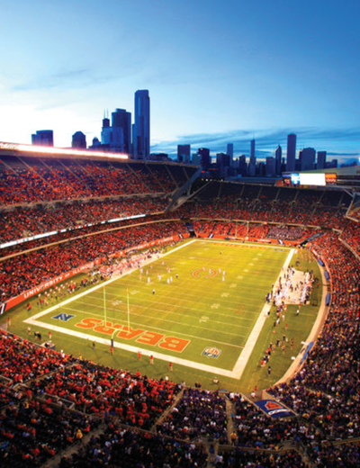 Football stadium at dusk with city skyline in background.