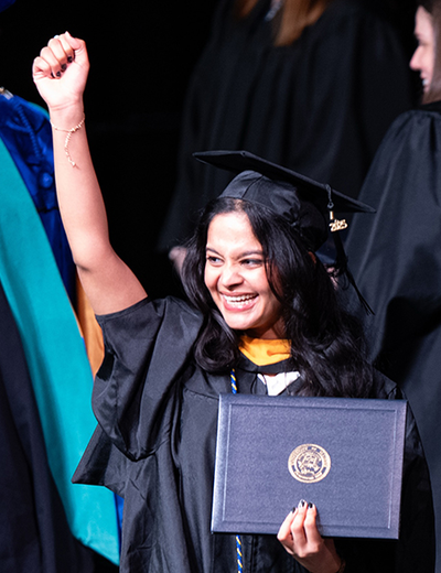Graduate smiling, holding diploma, raising fist on stage.