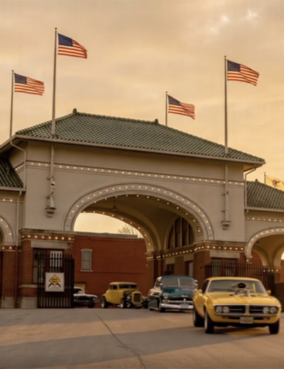 Historic gateway at sunset, vintage cars parked, flags waving.