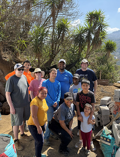 Group of people posing outdoors with trees and mountains in the background.