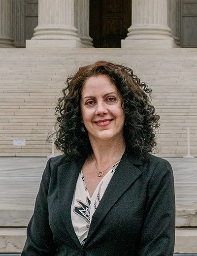 Woman in a suit smiling in front of a building with large steps.