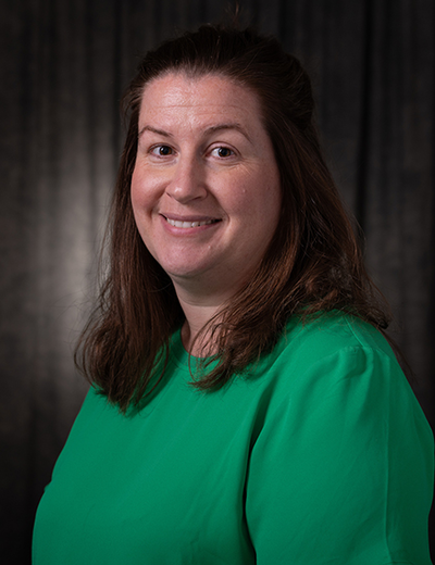 Smiling woman in a green shirt against a dark background.