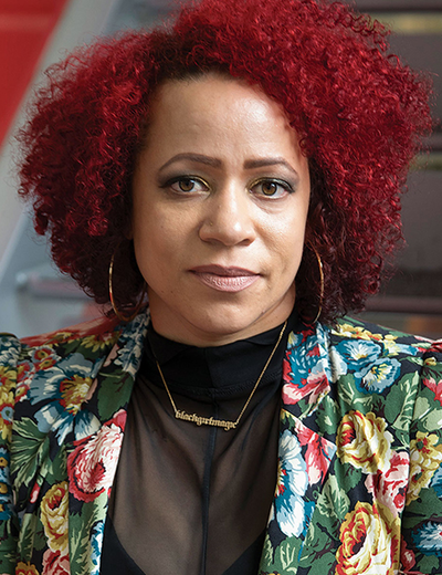 A woman with curly red hair, wearing a floral jacket and hoop earrings.