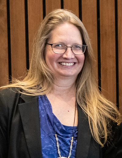 Smiling woman with long hair, wearing glasses and a blue top.