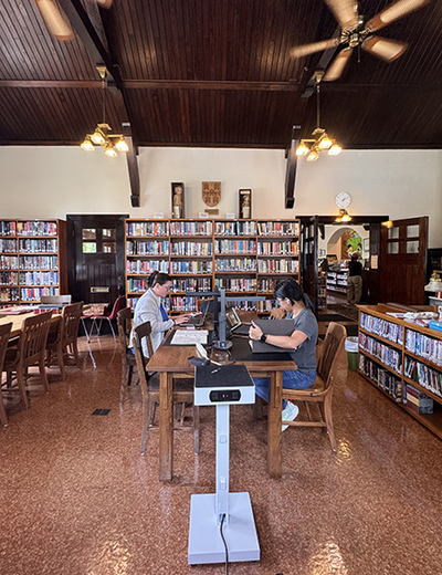 Cozy library with two people working at a wooden table, surrounded by bookshelves.