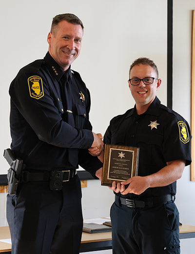 Two uniformed officers smiling as one receives a plaque.