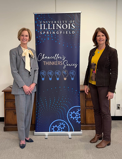 Two women standing beside University of Illinois Springfield banner indoors.