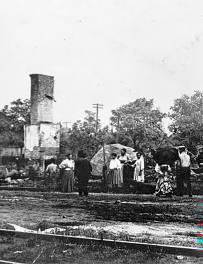People standing near a tall, damaged building with trees in the background.