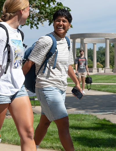 Students smiling, walking on grassy campus with backpacks.