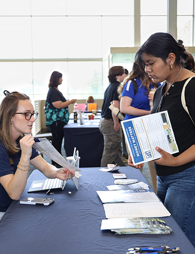Woman at table discussing brochures with an attendee at an event.