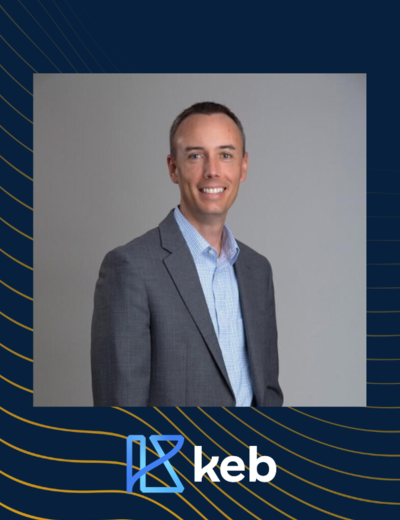 Smiling man in suit against gray background, with a blue logo and "keb" text below.