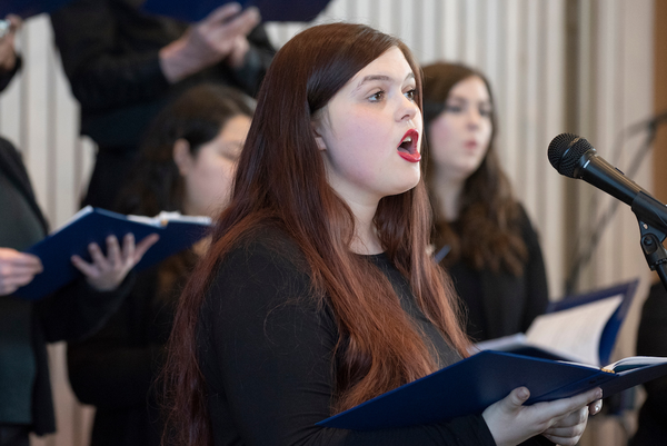 photograph of a woman singing with other singers behind her