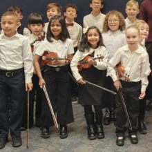 Children in white shirts holding violins and smiling.