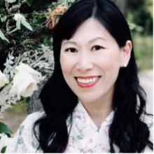 Smiling woman in floral dress near white roses outdoors.