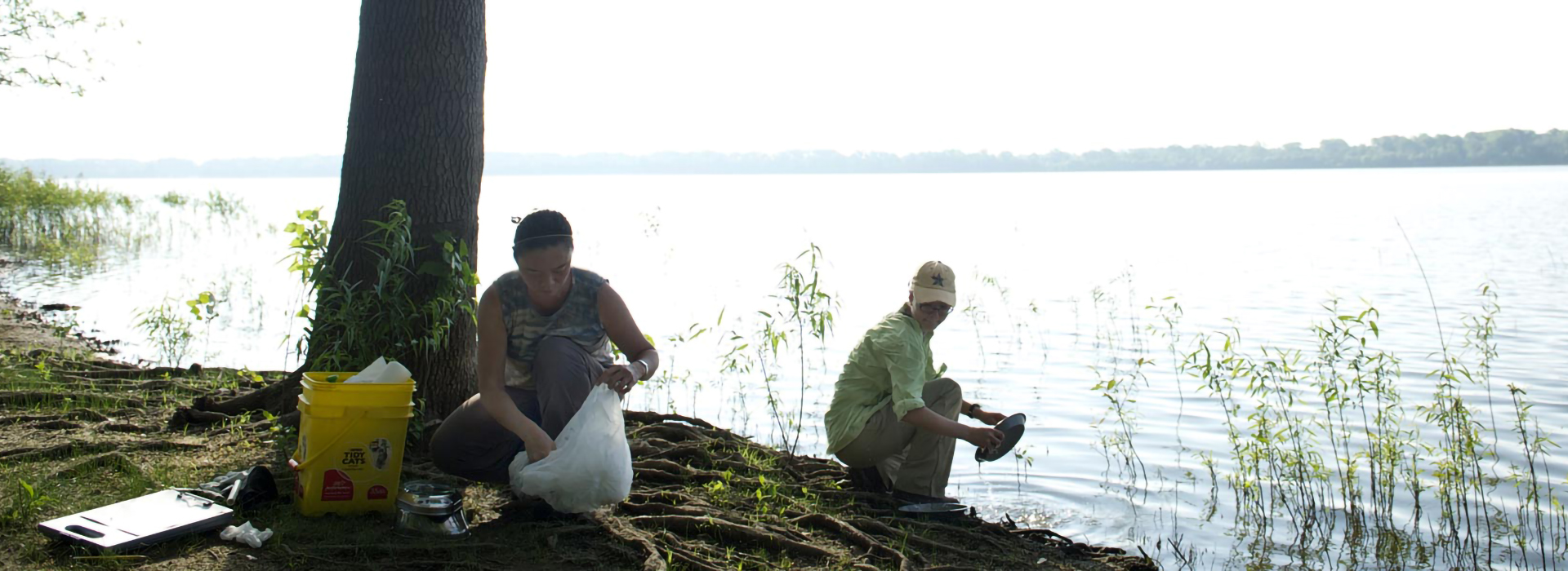 two people cleaning up garbage near a lake