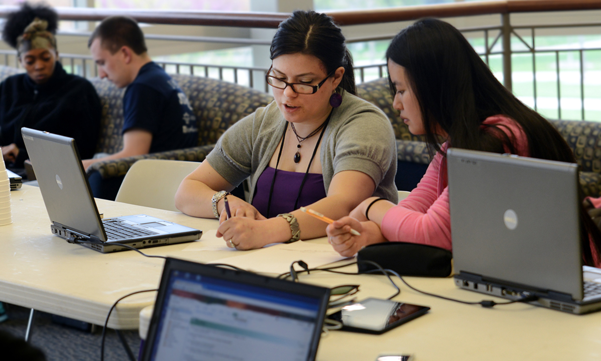 Two tutors and two students work together in two separate meetings with computers strewn about