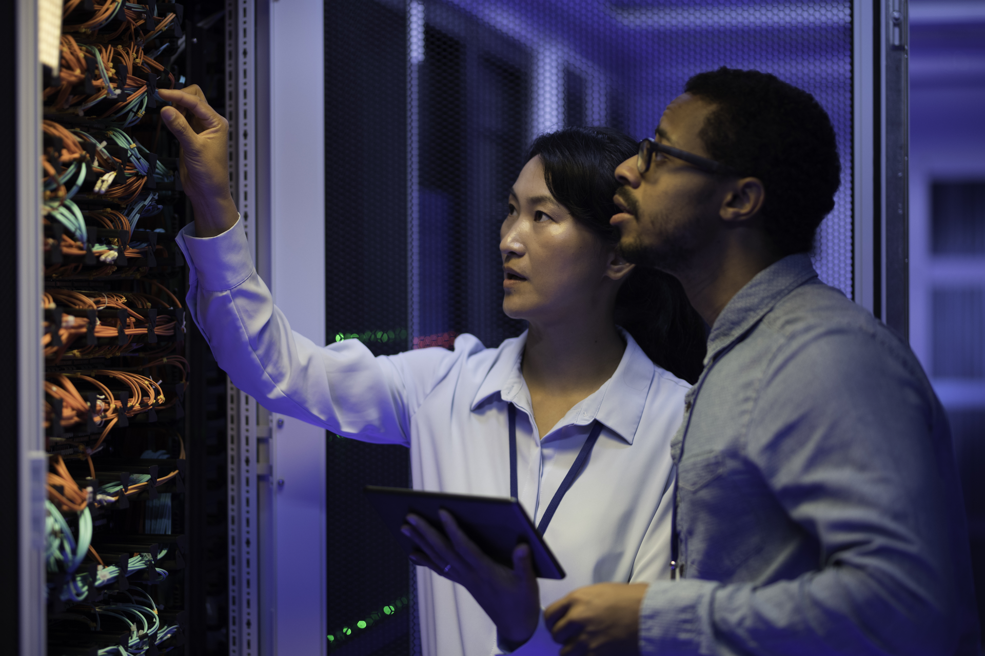 An Asian woman and African American man look a computer server with wires and lights. 