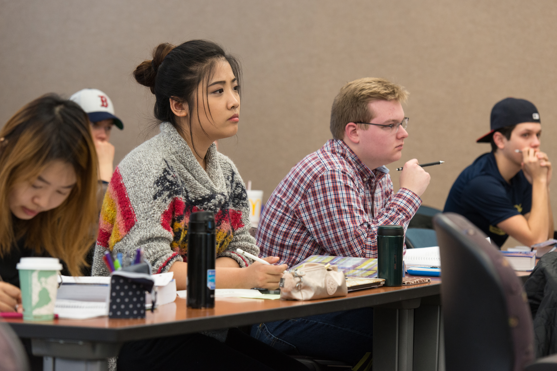 Two young men and two young women sit at a table, notes and pens in hand in a classroom setting.