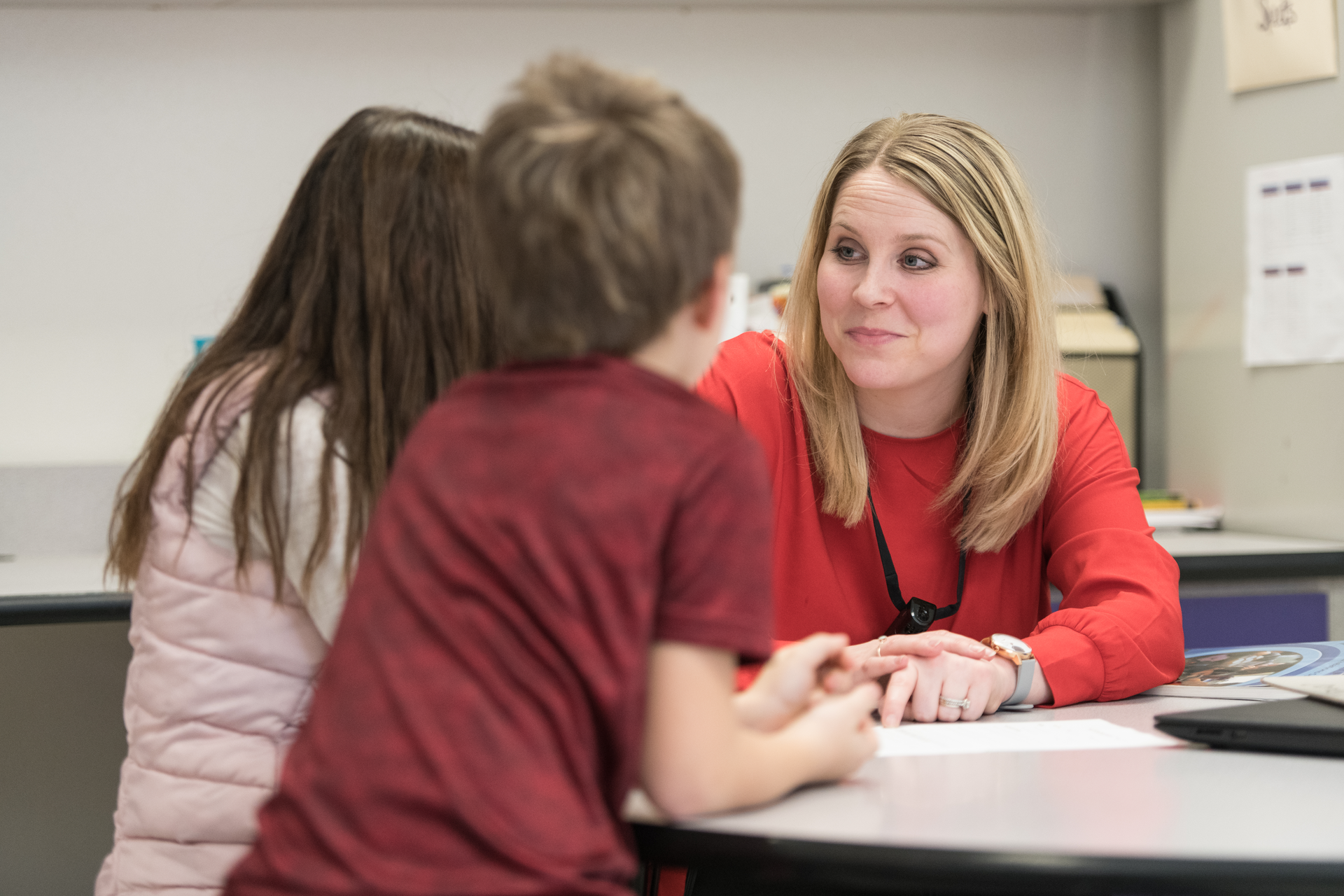 Blonde woman talks with two elementary age students in a classroom setting.
