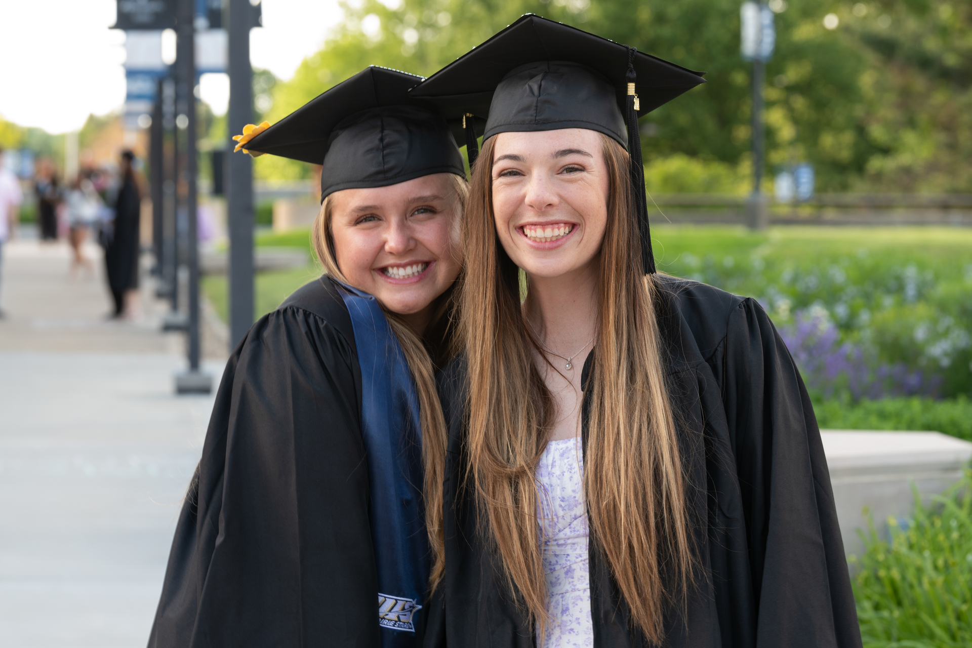 Two UIS graduates pose outside while wearing their cap and gowns