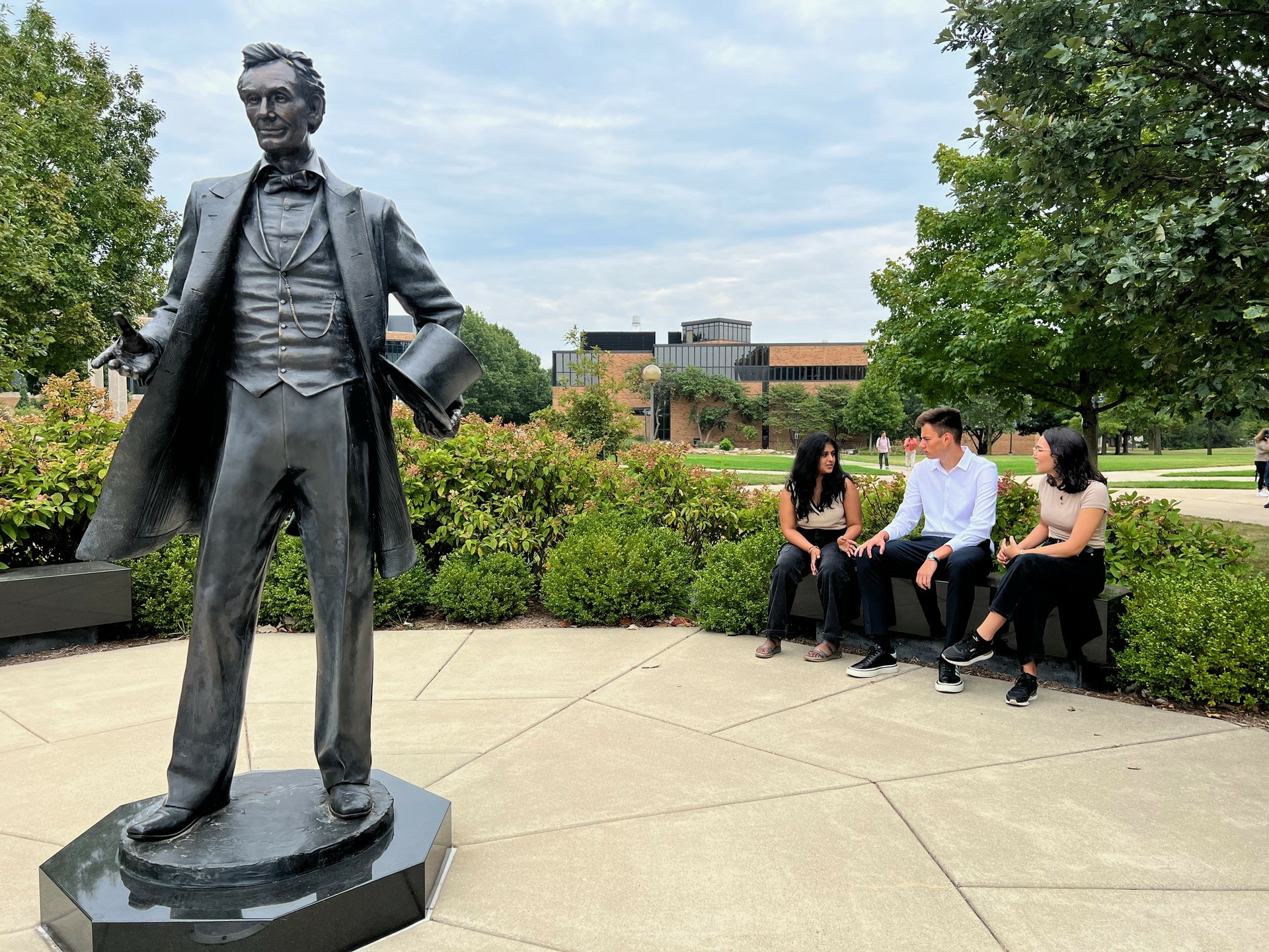 A group of students talking while sitting on a bench. There is a statue of Abraham Lincoln on the left hand side.