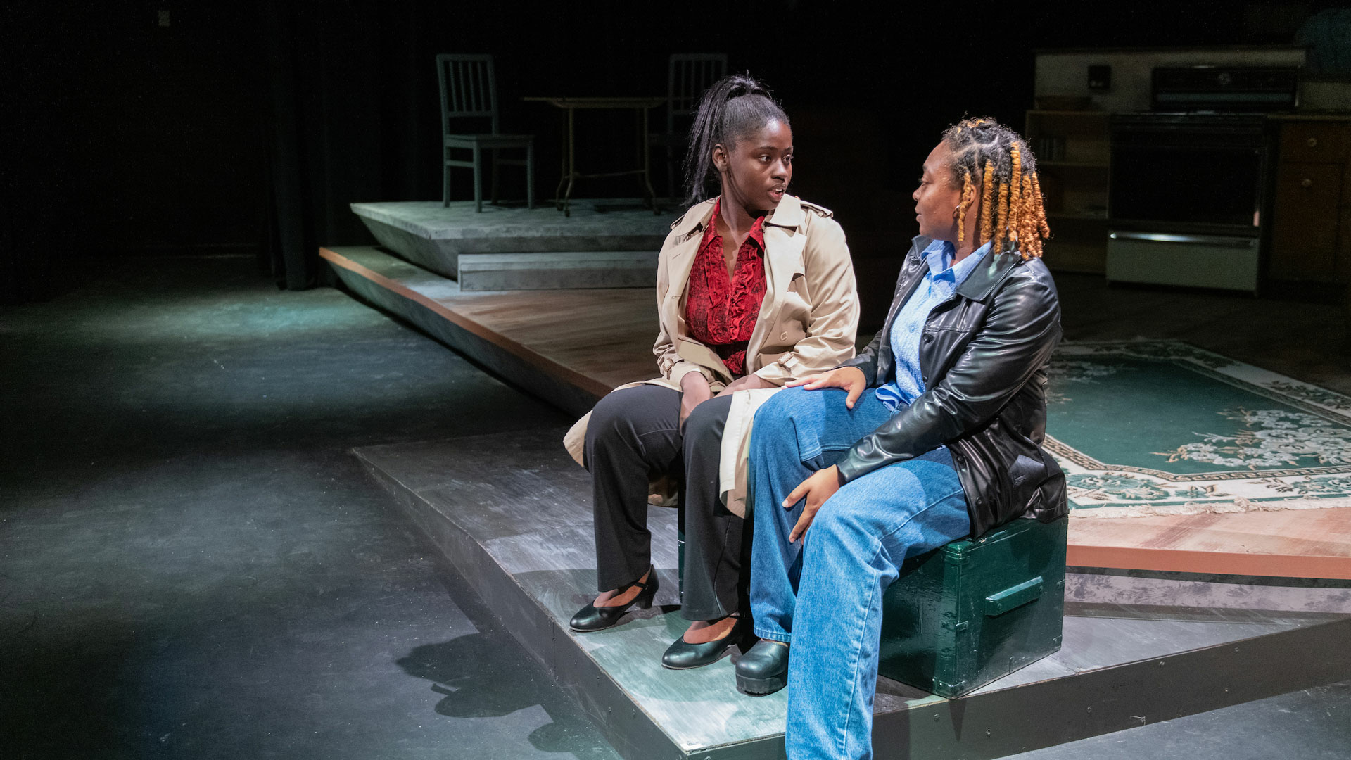 two people sitting on stage in a play talking to each other