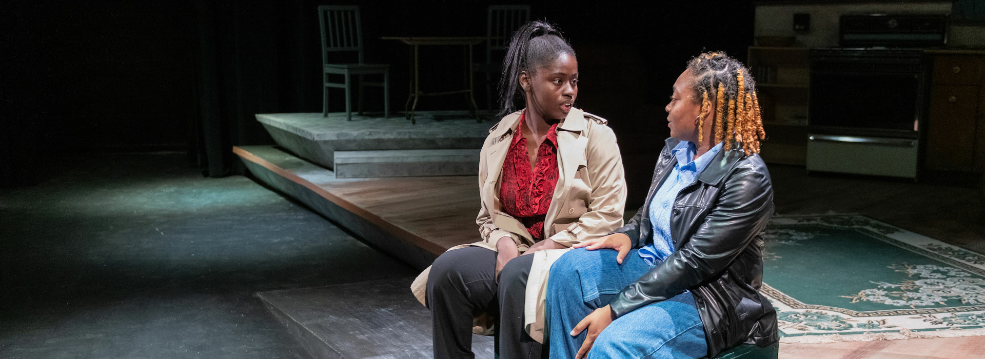 two people sitting on stage in a play talking to each other