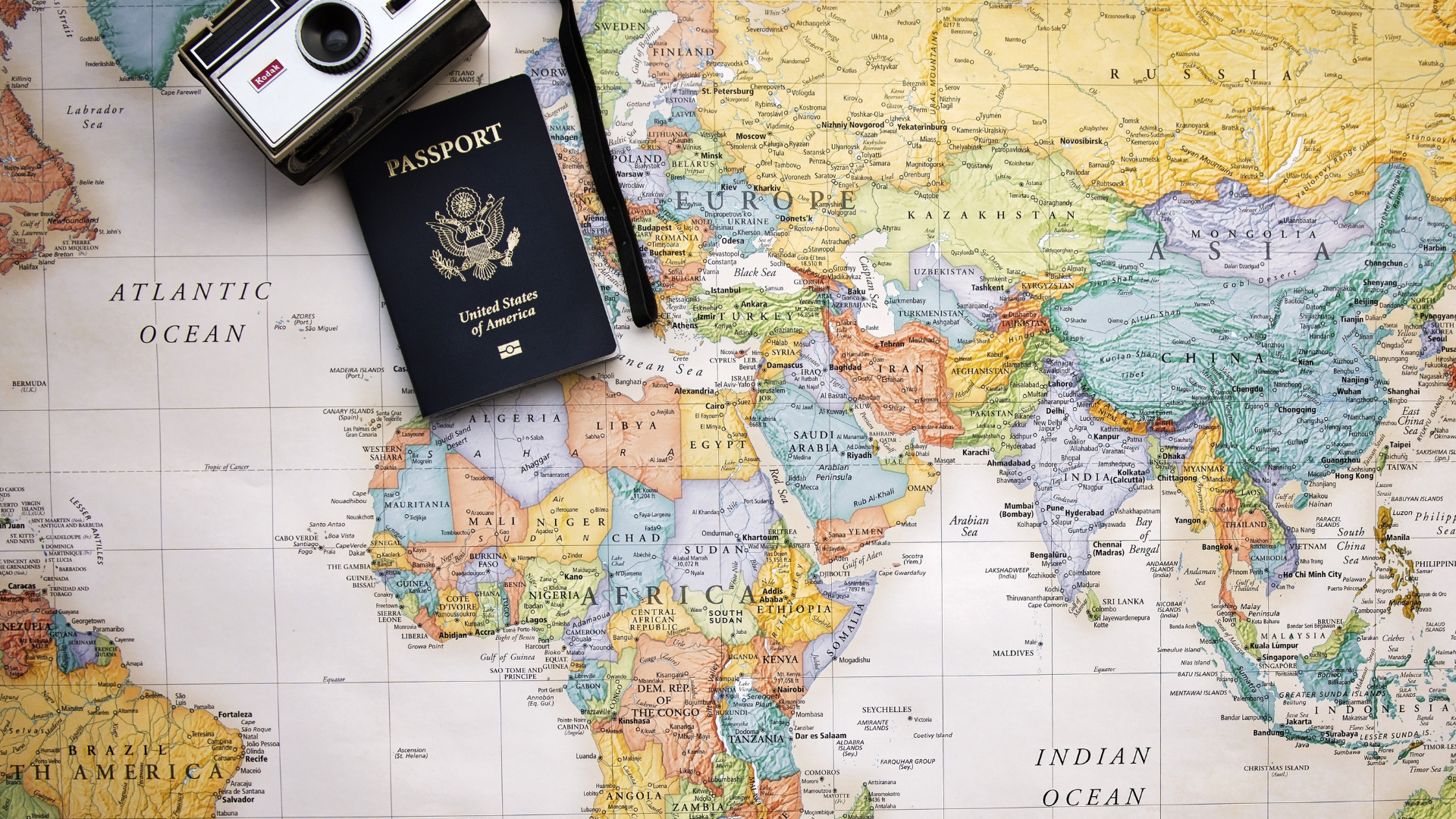 A colorful world map with a United States passport and silver film camera laying on it.
