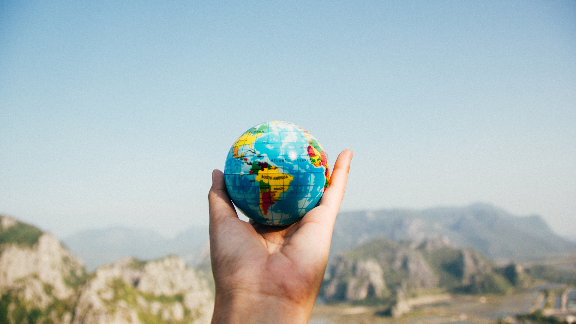 hand holding up an apple-sized world globe. The background consists of out of focus rock formations.
