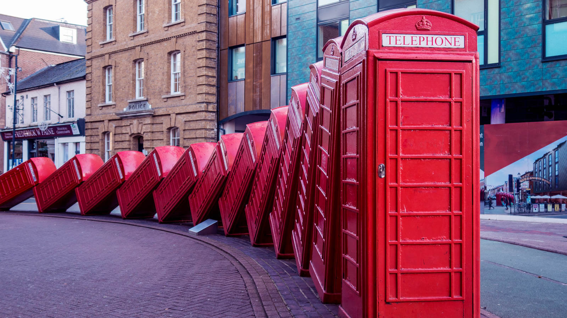 Line of red British telephone booths falling over like dominos from the left.