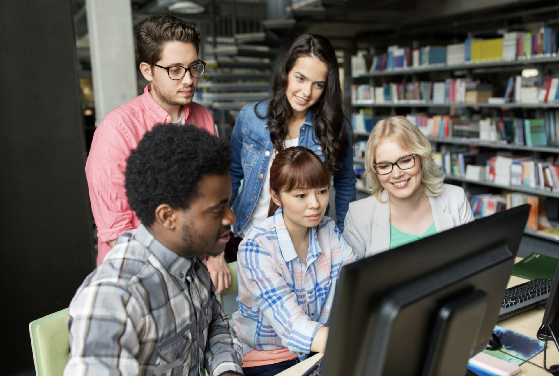 5 members's looking at a computer or a desktop in the library space 