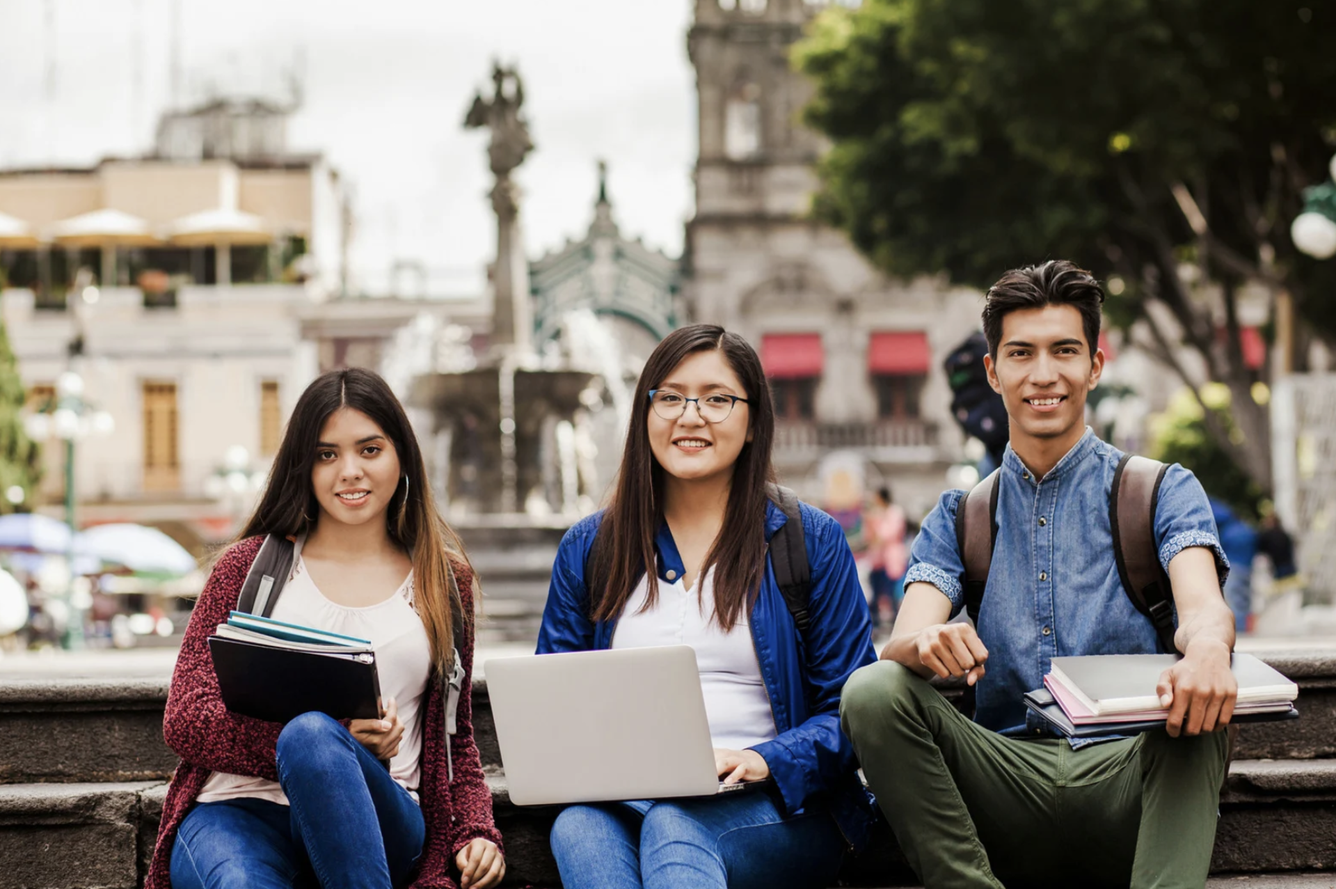 3 student's sitting in a public space with laptops and some books in the hand