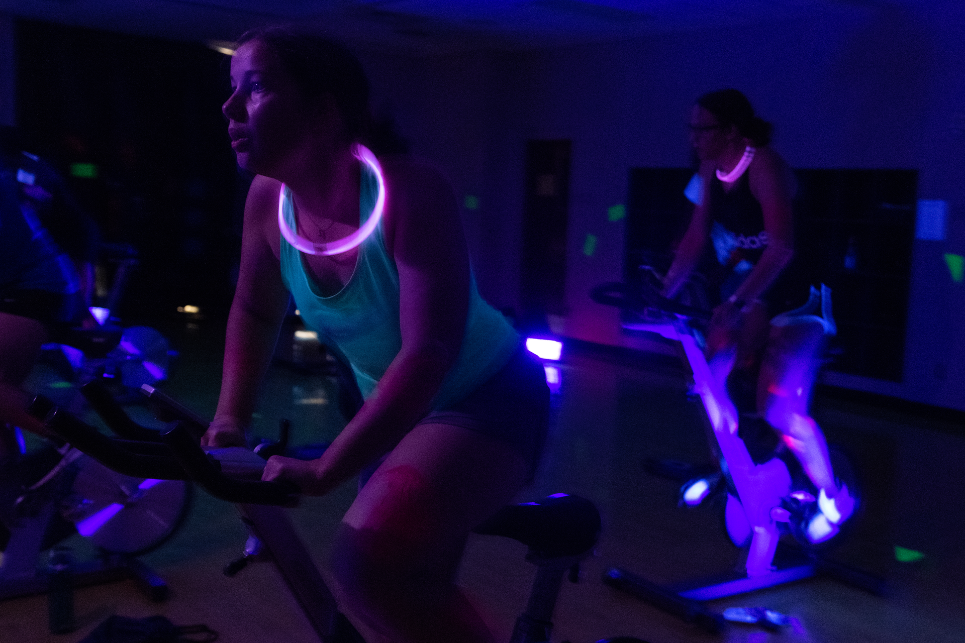 Students on cycling bikes in a glow in the dark room with glow sticks around their necks. 