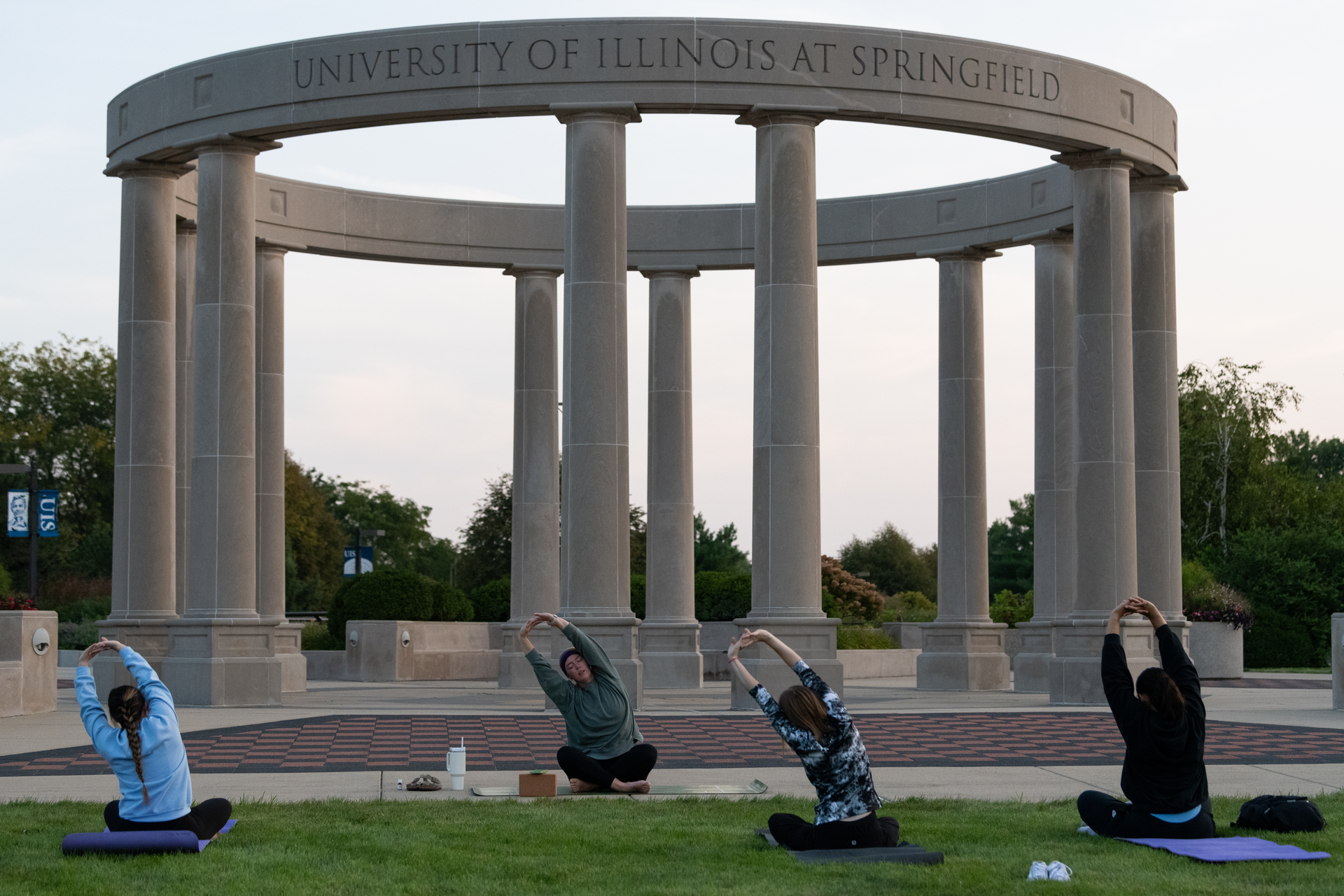 Three students and a yoga instructor doing yoga on the quad in front of the colonnade