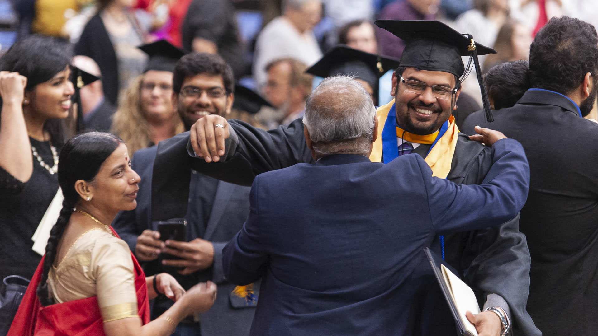 a male graduate in cap and gown hugging his father