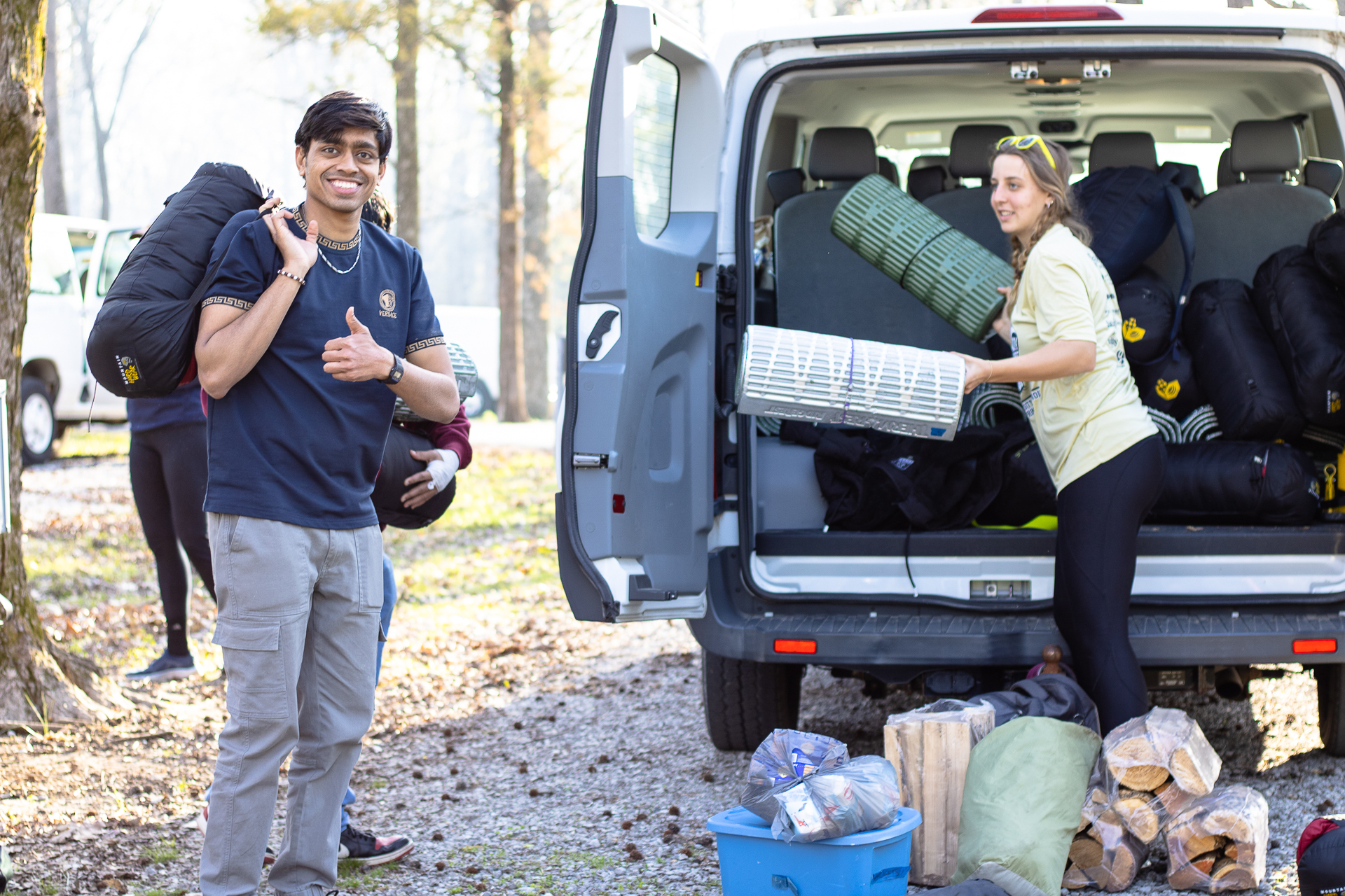Students unpacking camping equipment from van and one student giving a thumbs up.
