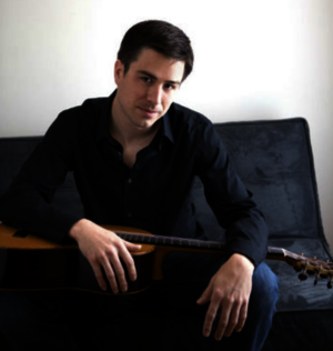 UIS faculty member Adam Larison sitting and holding a guitar