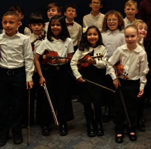 Children in white shirts holding violins and smiling.