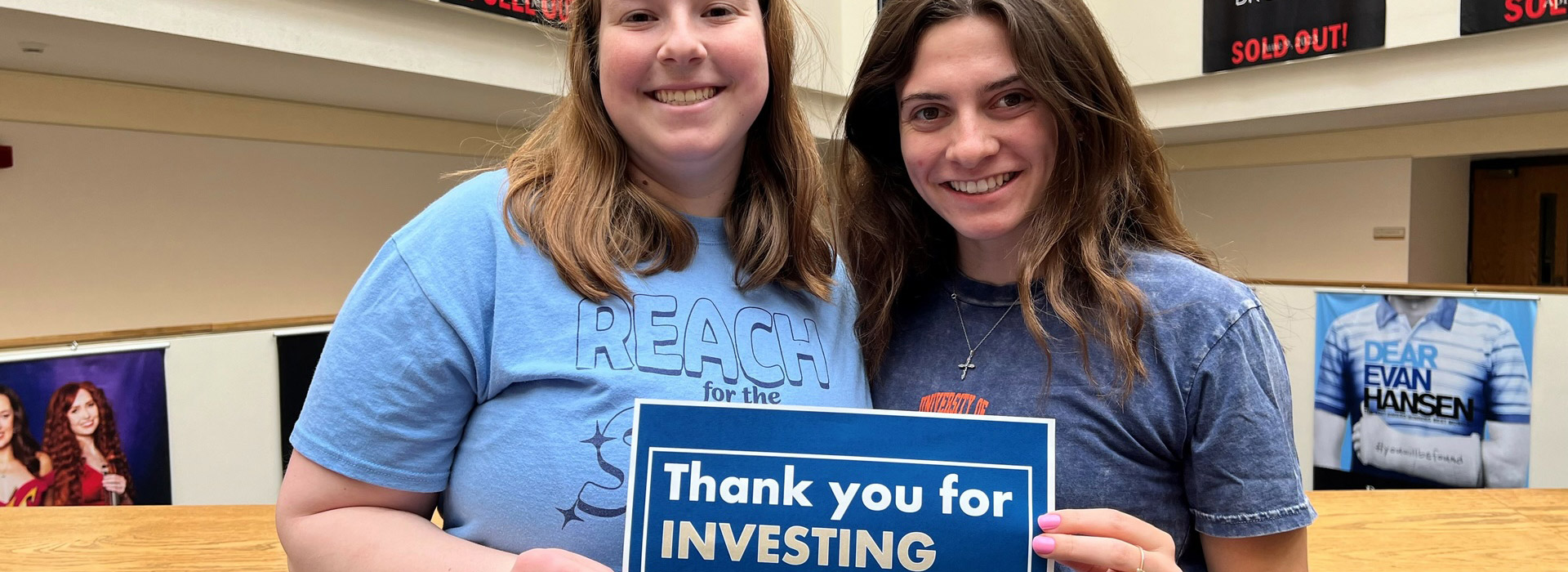 two students holding up a sign that reads "thank you for INVESTING in me"